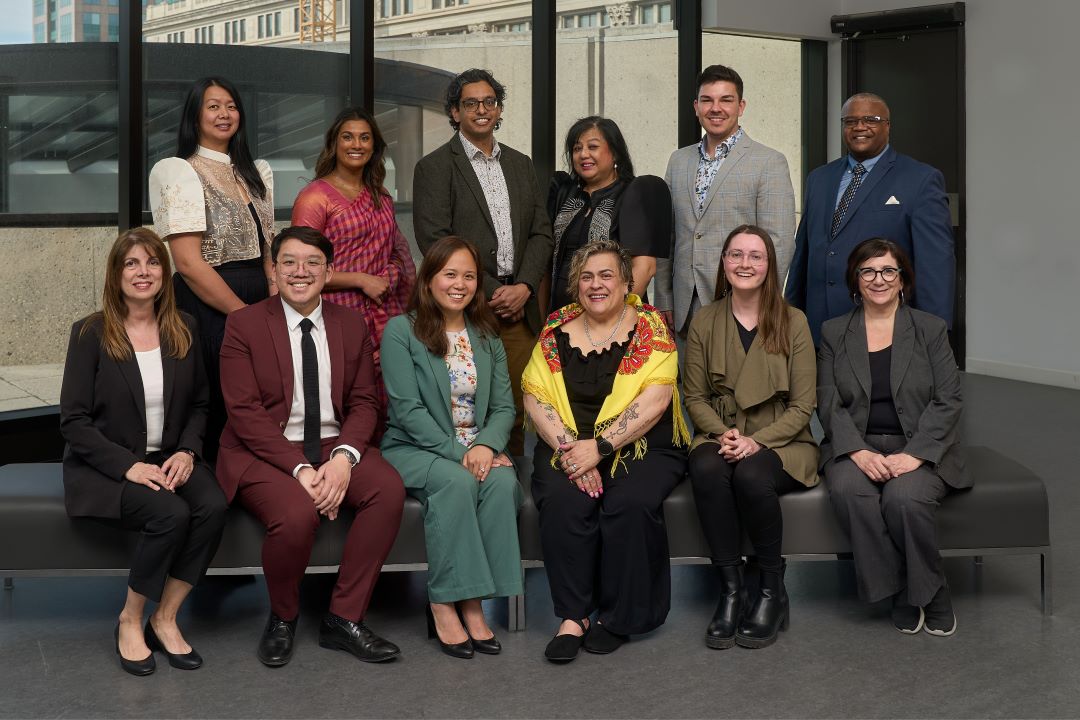 A diverse group of professionals post for a photo. Half are seated, half stand behind them.